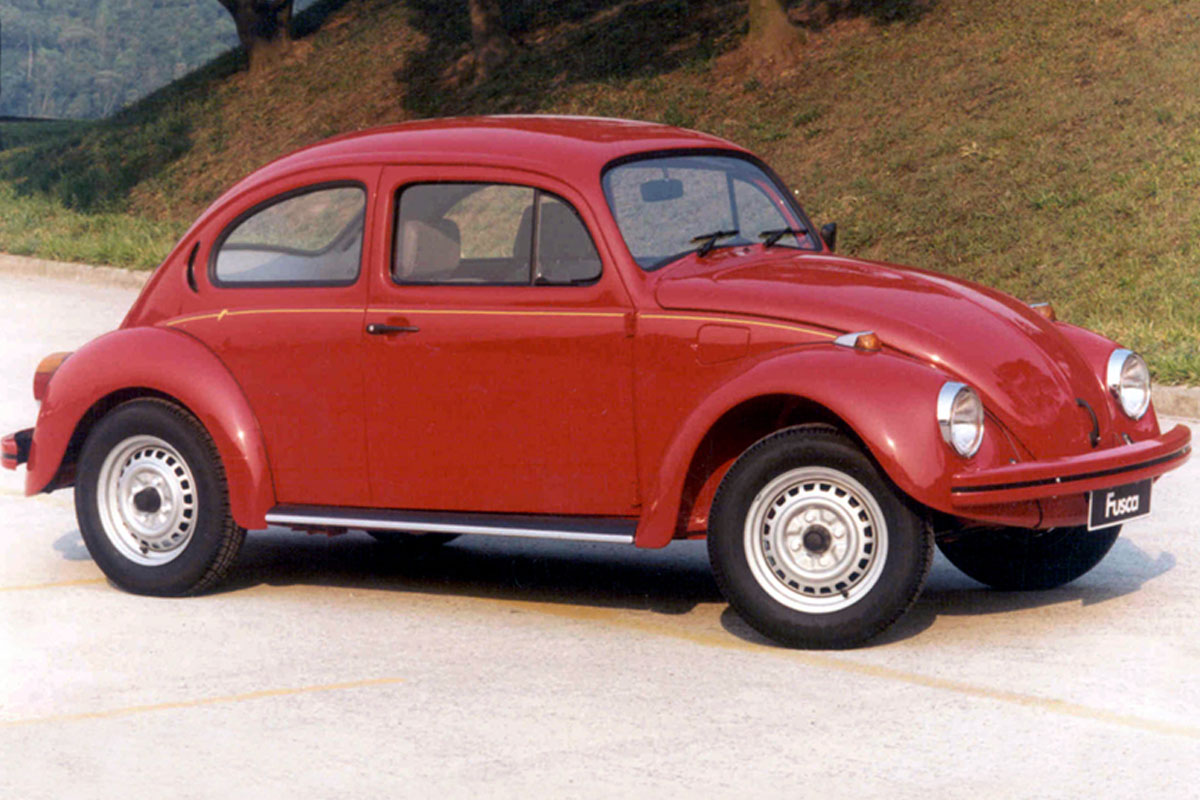 Volkswagen Fusca Série Ouro vermelho em foto de lateral no asfalto com plantas ao fundo