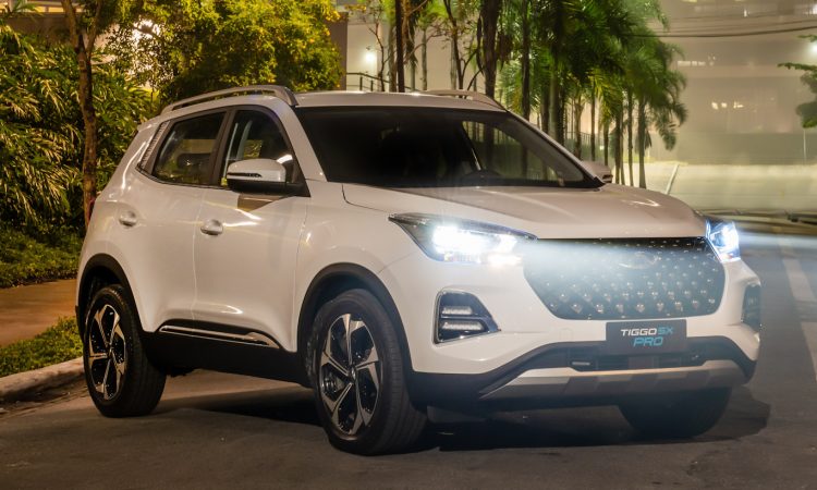 CAOA Chery Tiggo 5X Pro Hybrid branco com faróis acesos em frente a um Shopping