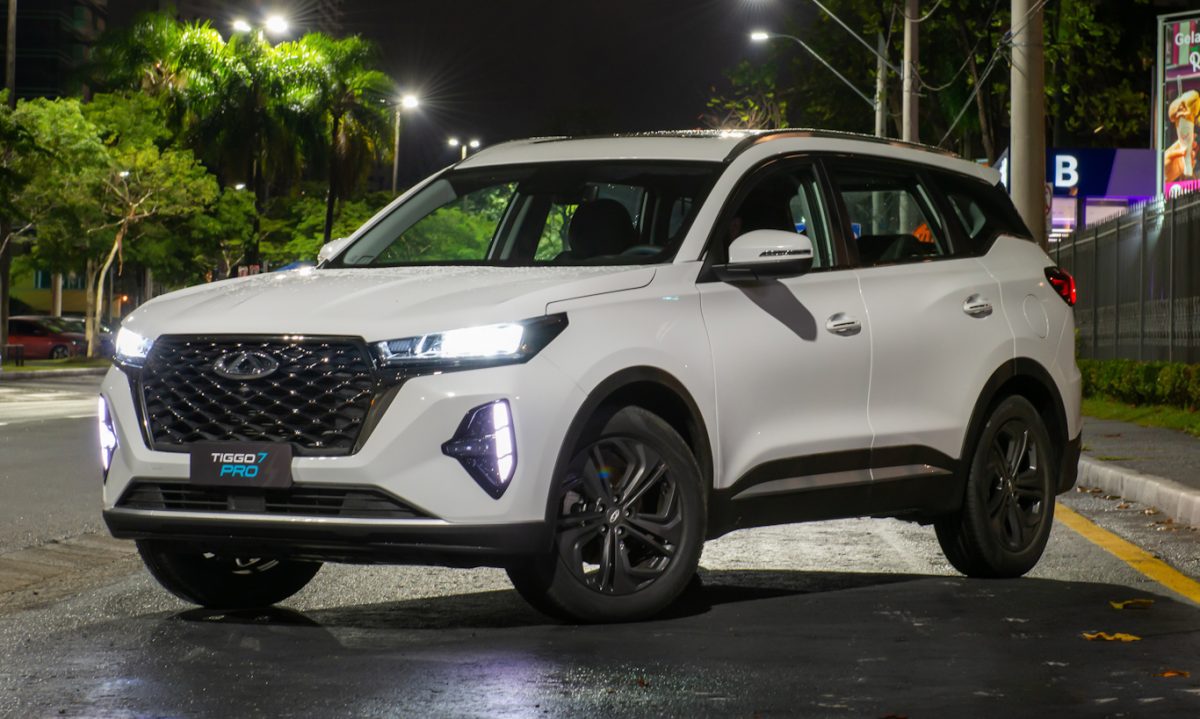 CAOA Chery Tiggo 7 Pro Hybrid branco parado de frente a noite em um estacionamento com os faróis acesos