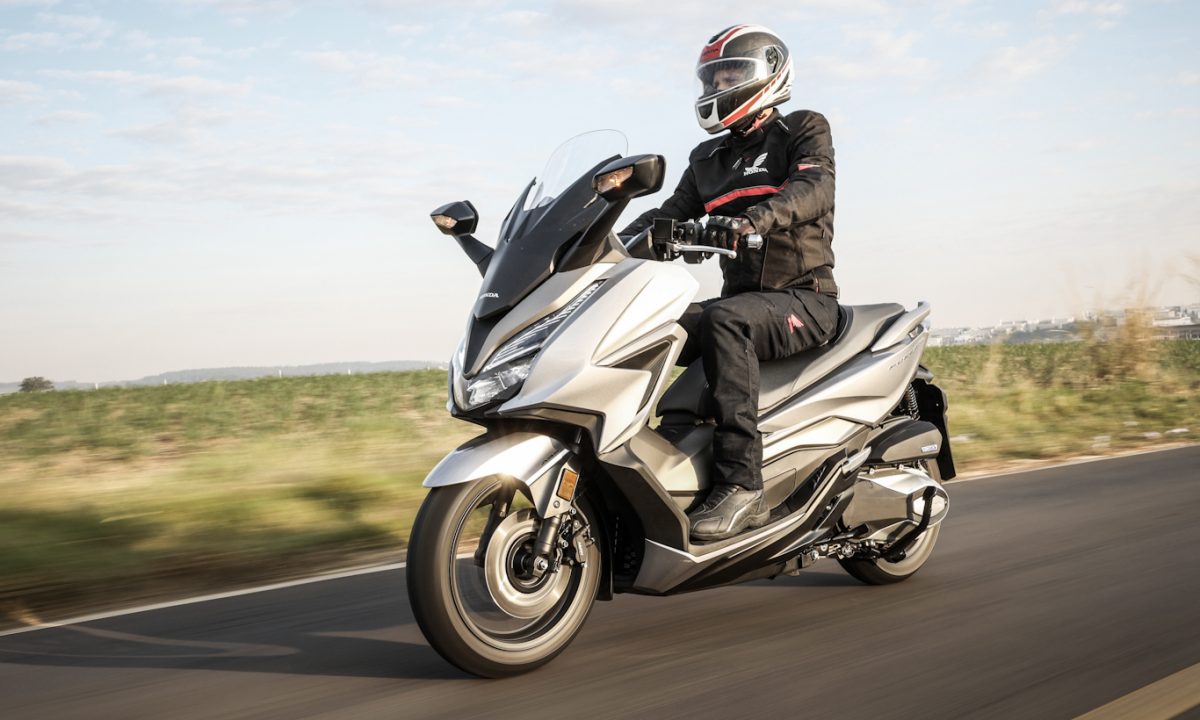 Maxi-Scooter Honda Forza 350 cinza andando no asfalto com paisagem ao fundo 