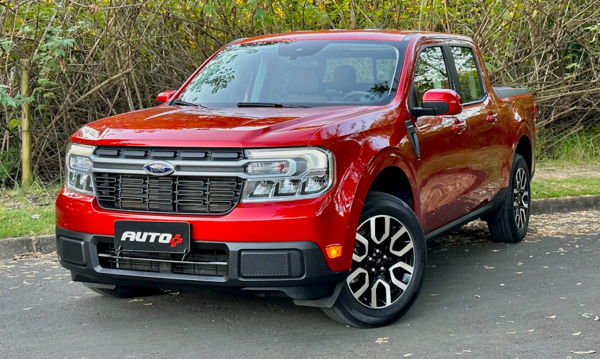 Ford Maverick Hybrid vermelha usa a eletrificação e está estacionada de frente no asfalto com plantas ao fundo