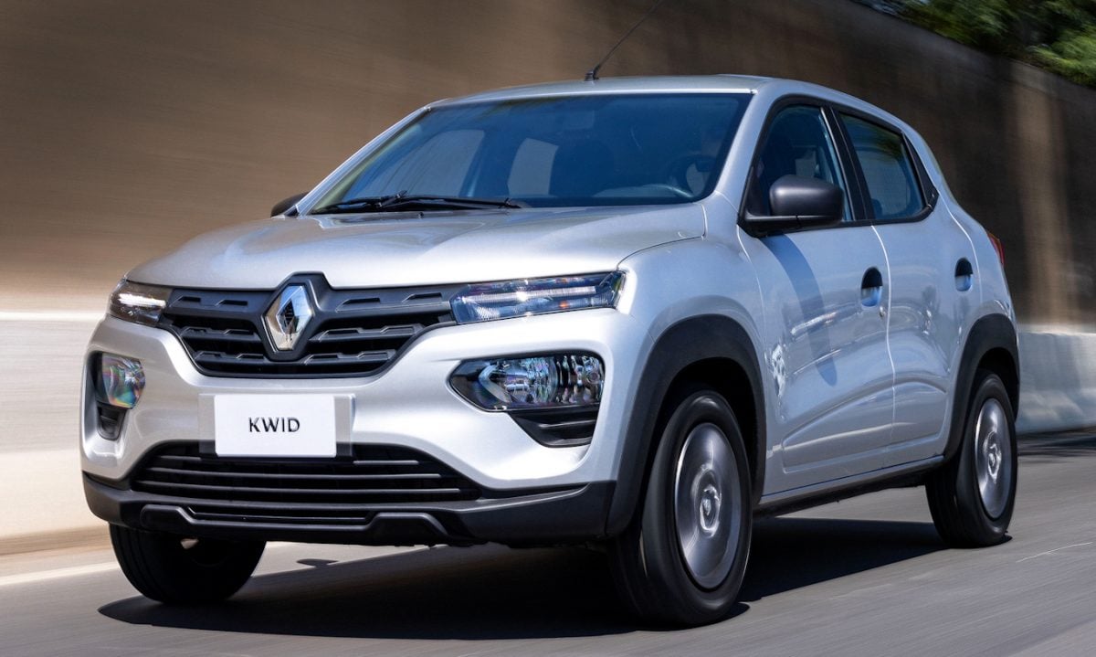 Os subcompactos são um tipo de carro que não agradam a todos os consumidores e o Renault Kwid prata de frente está andando na cidade com muro ao fundo
