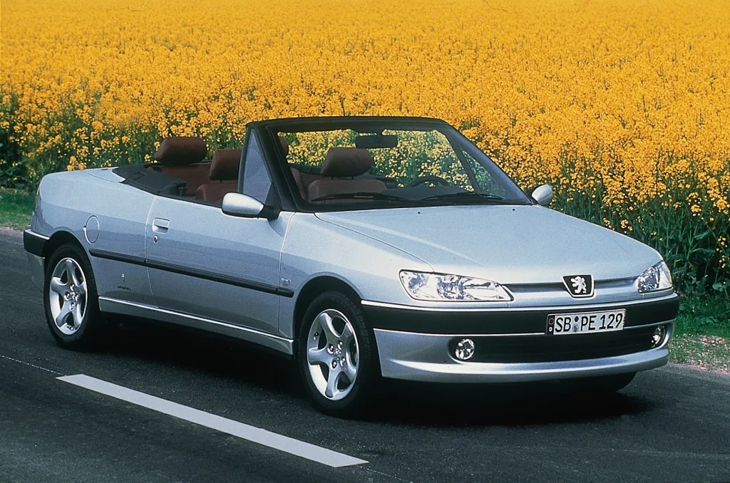 o design Pininfarina do Peugeot 306 Cabriolet prata com a capota aberta na estrada com flores amarelas ao fundo