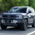 Fang Cheng Bao 5 azul em foto de movimento na estrada de asfalto com plantas ao fundo