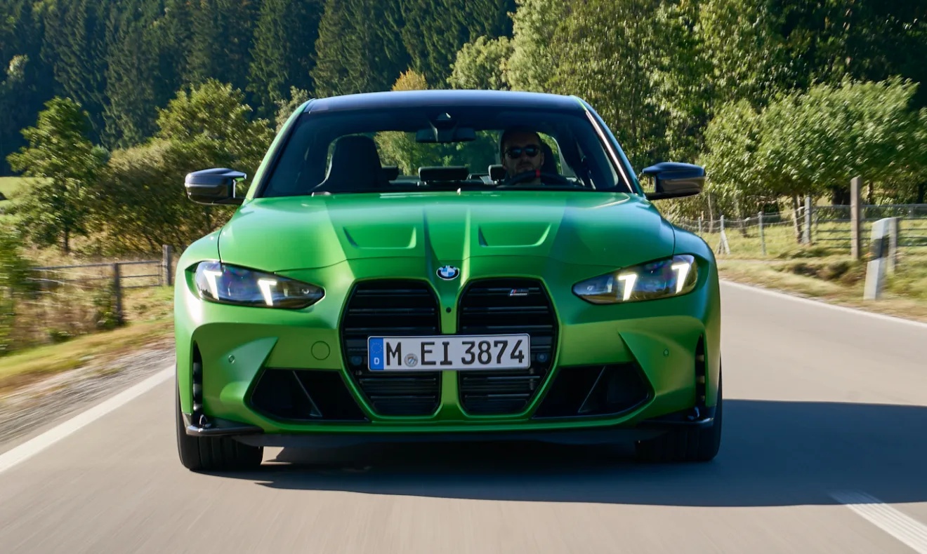 Novo BMW M3 Competition Track verde em foto de dianteira na estrada com árvores no fundo