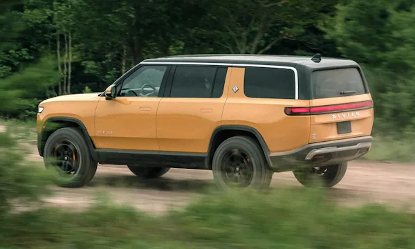 Rivian R1S amarelo andando rápido pela floresta e areia de traseira