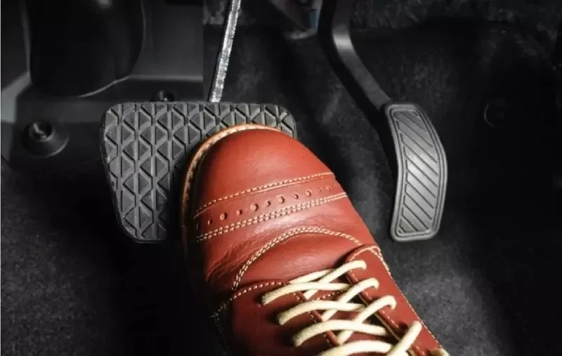 pedais de um carro e um sapato amarronzado pisando no freio - Técnicas de como ecomizar combústivel na estrada