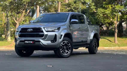 Toyota Hilux SRX Plus prata parada de frente em um estacionamento com uma floresta ao fundo