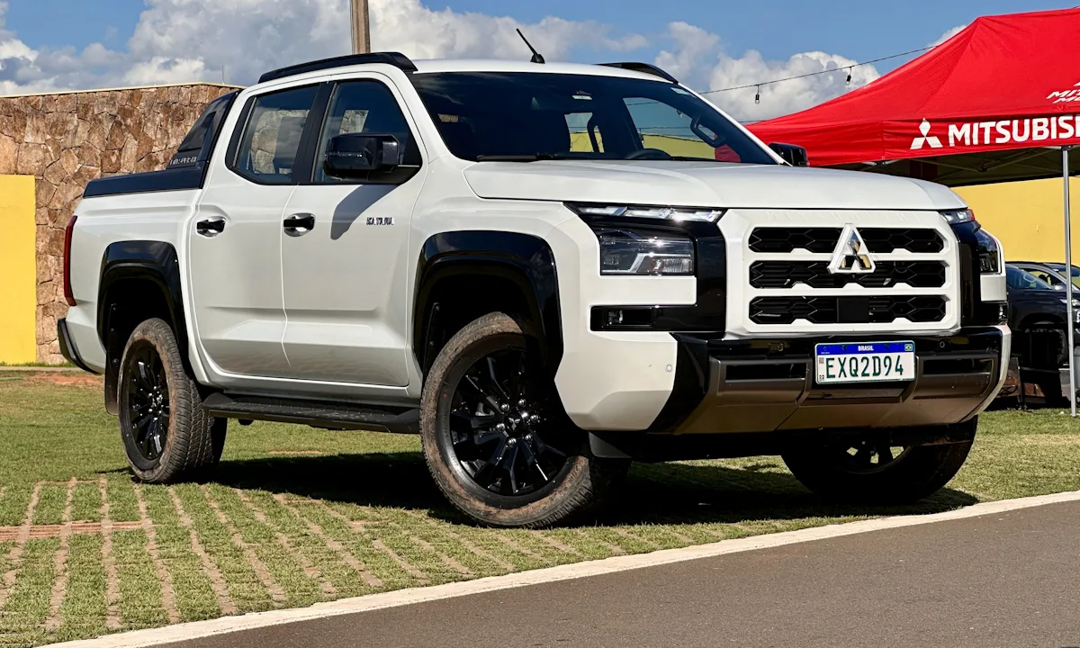 Mitsubishi Triton Katana branca com detalhes pretos com uma tenda vermelha da Mitsubishi ao fundo