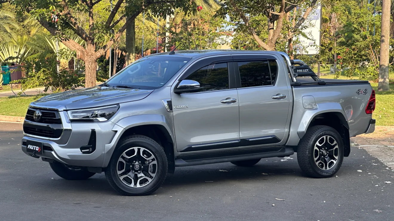 Toyota Hilux SRX Plus prata parada de levemente de lado em um estacionamento com uma floresta ao fundo