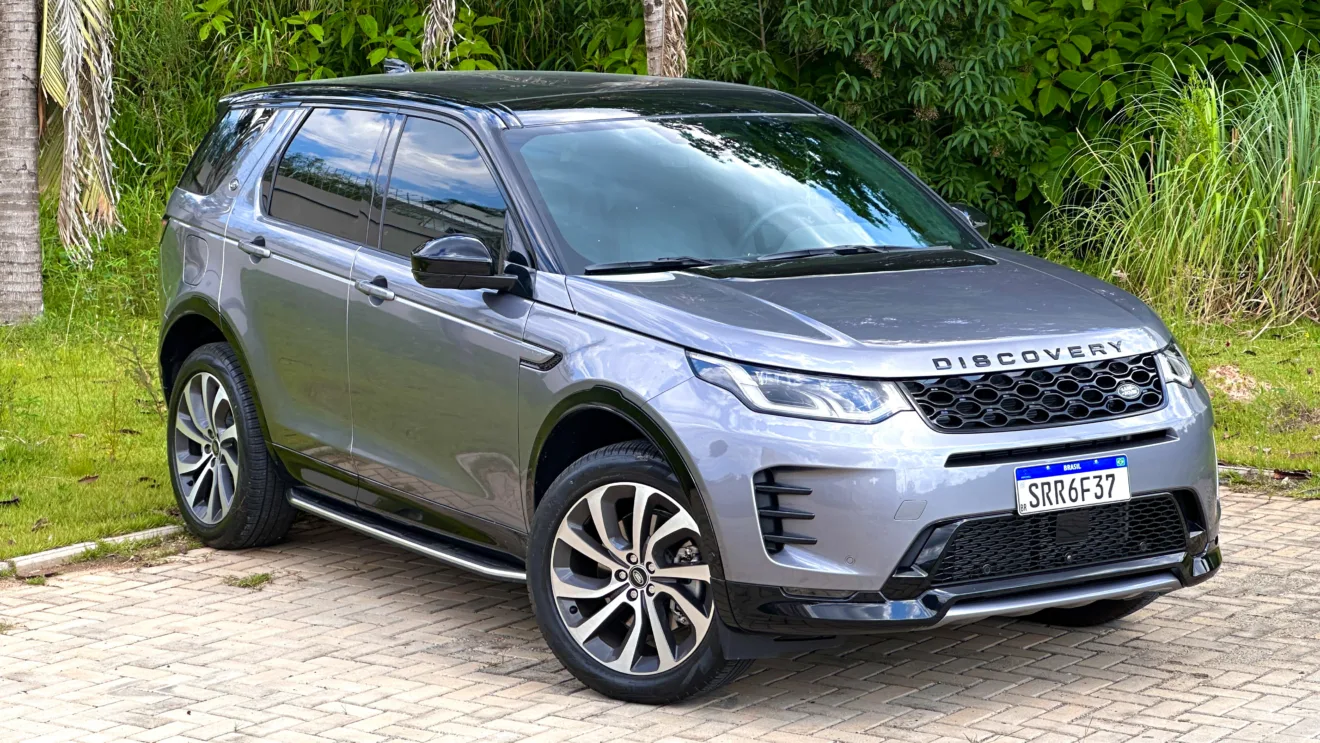 Land Rover Discovery Sport SE Dynamic flex cinza com teto preto parado em frente a um matagal