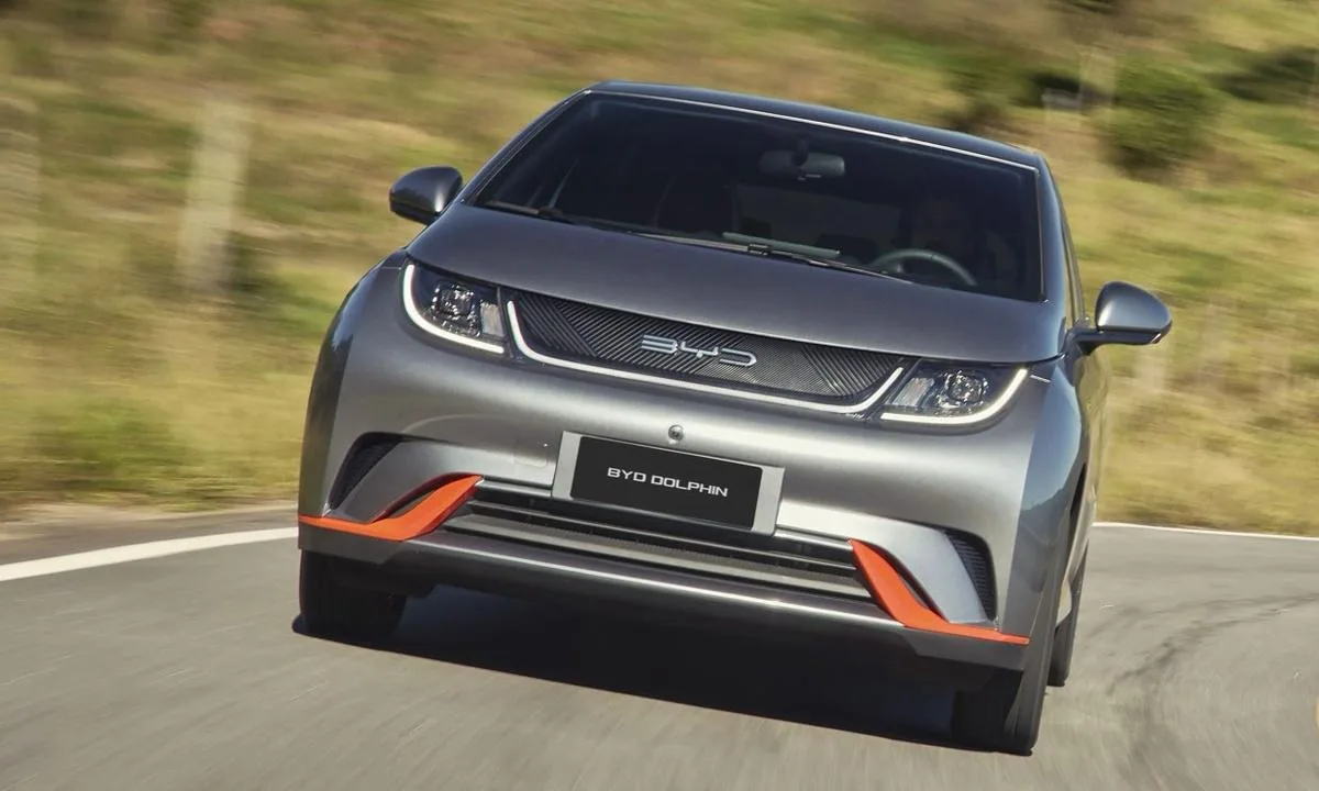 BYD Dolphin cinza com detalhes em laranja no para-choque dianteiro andando na estrada