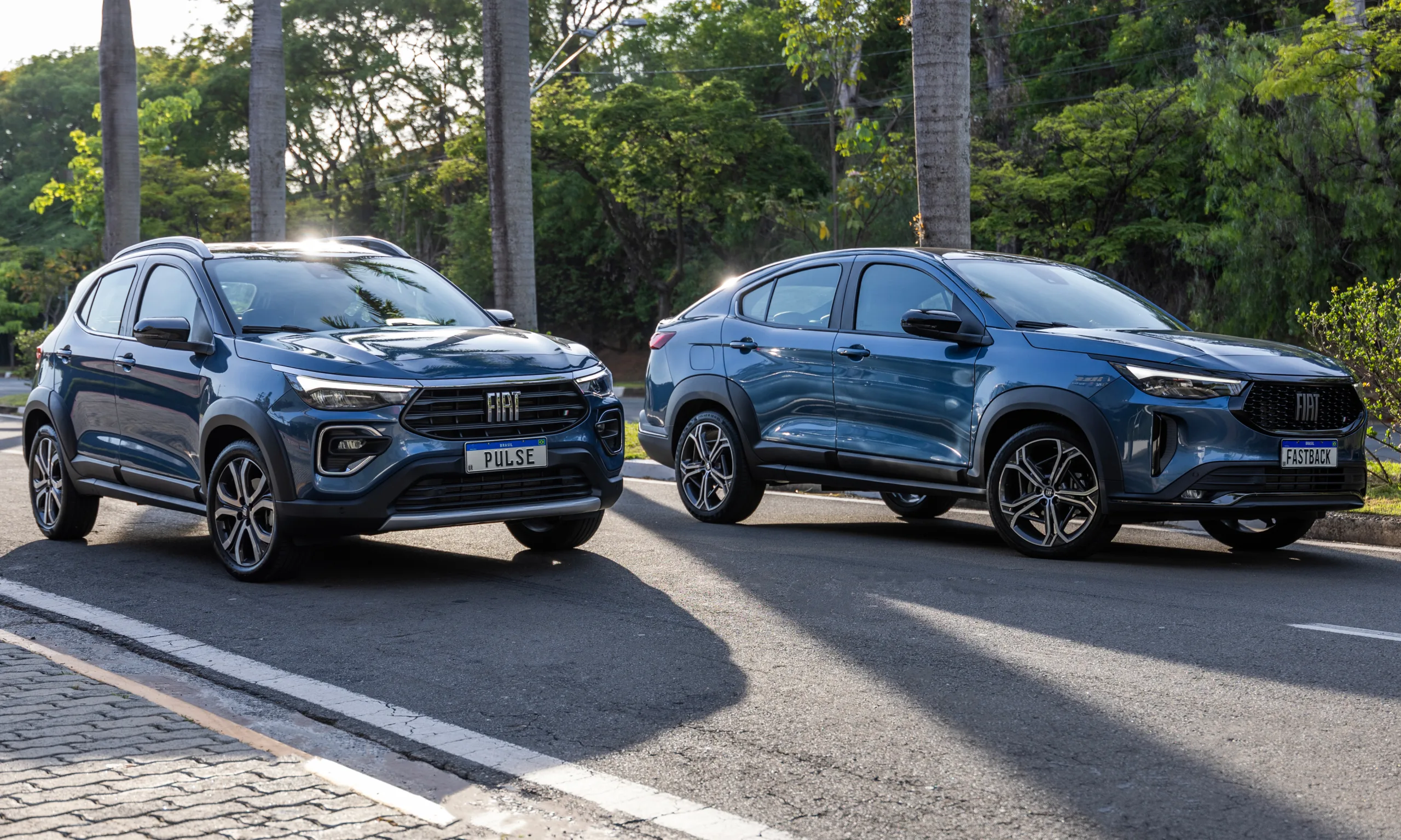 Fiat Pulse e Fastback Impetus híbridos-leve azuis vistos de frente e com plantas ao redor