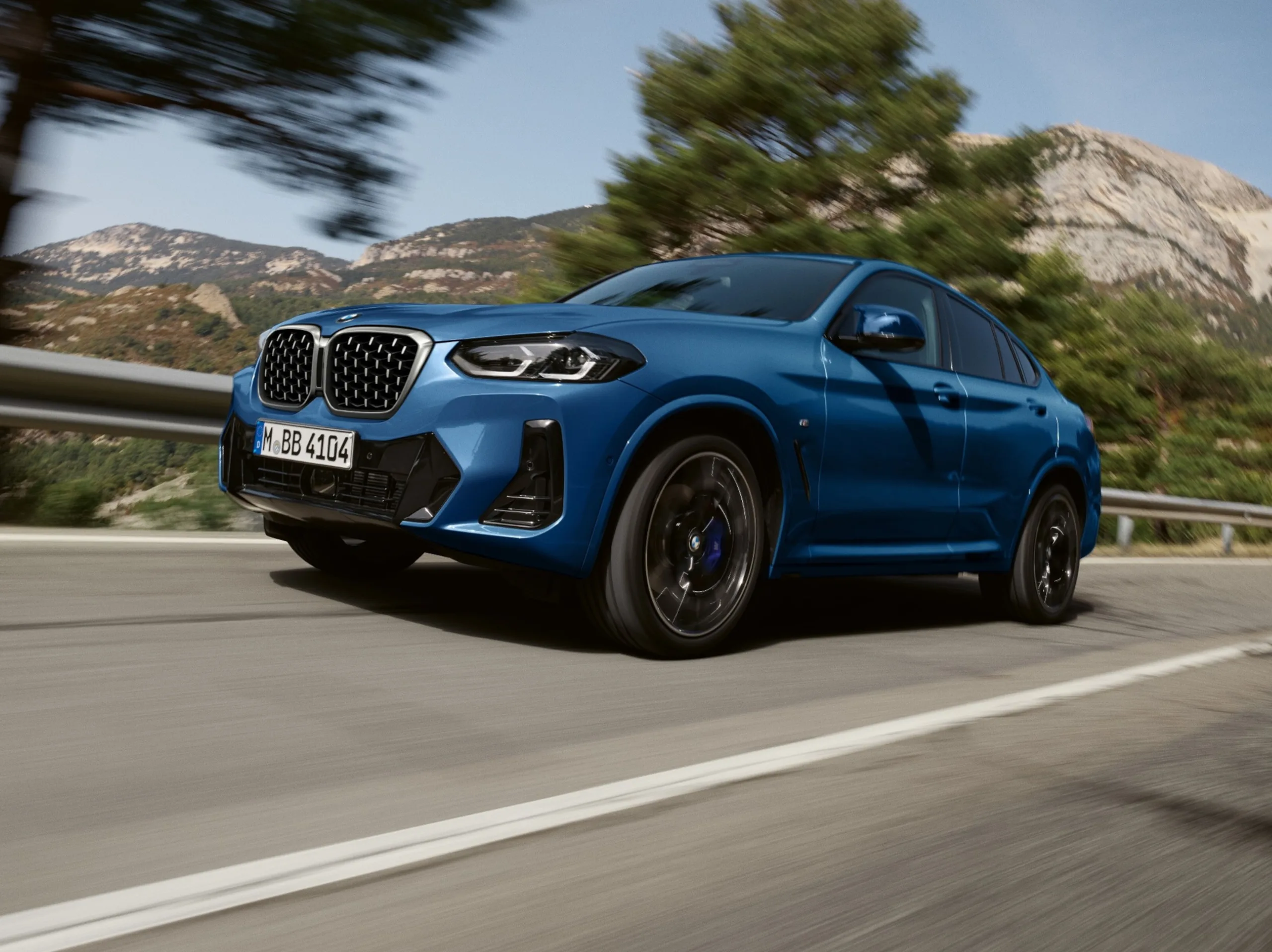 SUV BMW X4 xDrive20i M Sport azul andando na estrada e no asfalto com árvores ao fundo