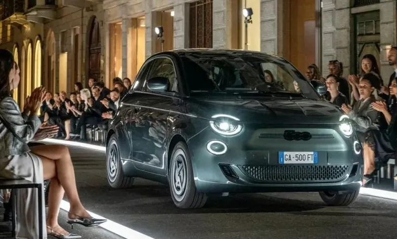 Fiat 500e Giorgio Armani verde, parado de frente em uma passarela, com faróis acesos e pessoas ao redor