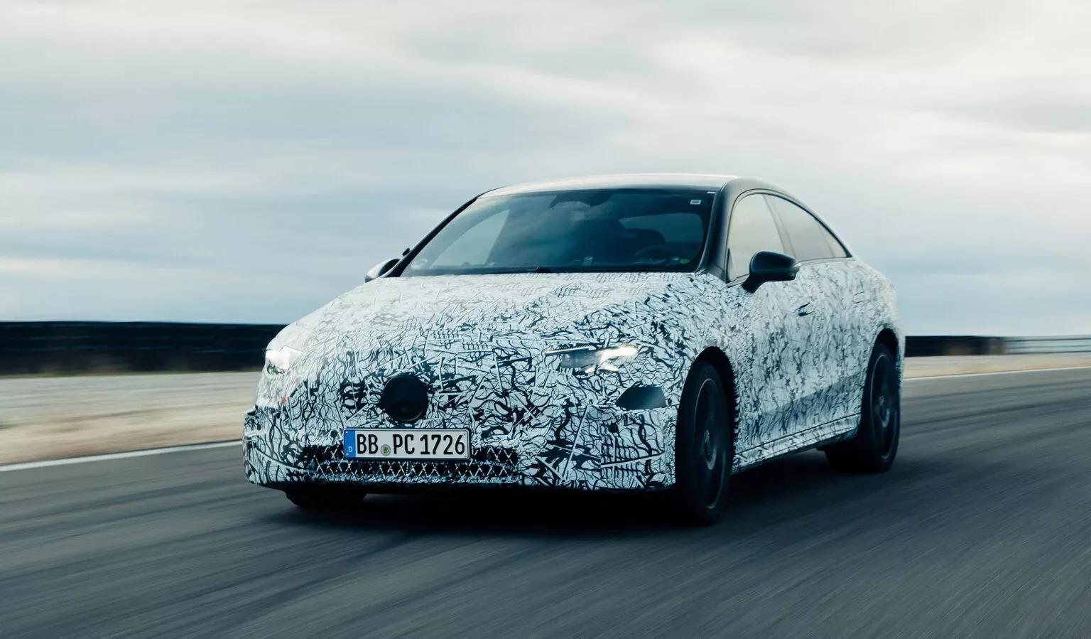 Novo Mercedes-Benz CLA camuflado de frente andando na pista com o céu nublado ao fundo