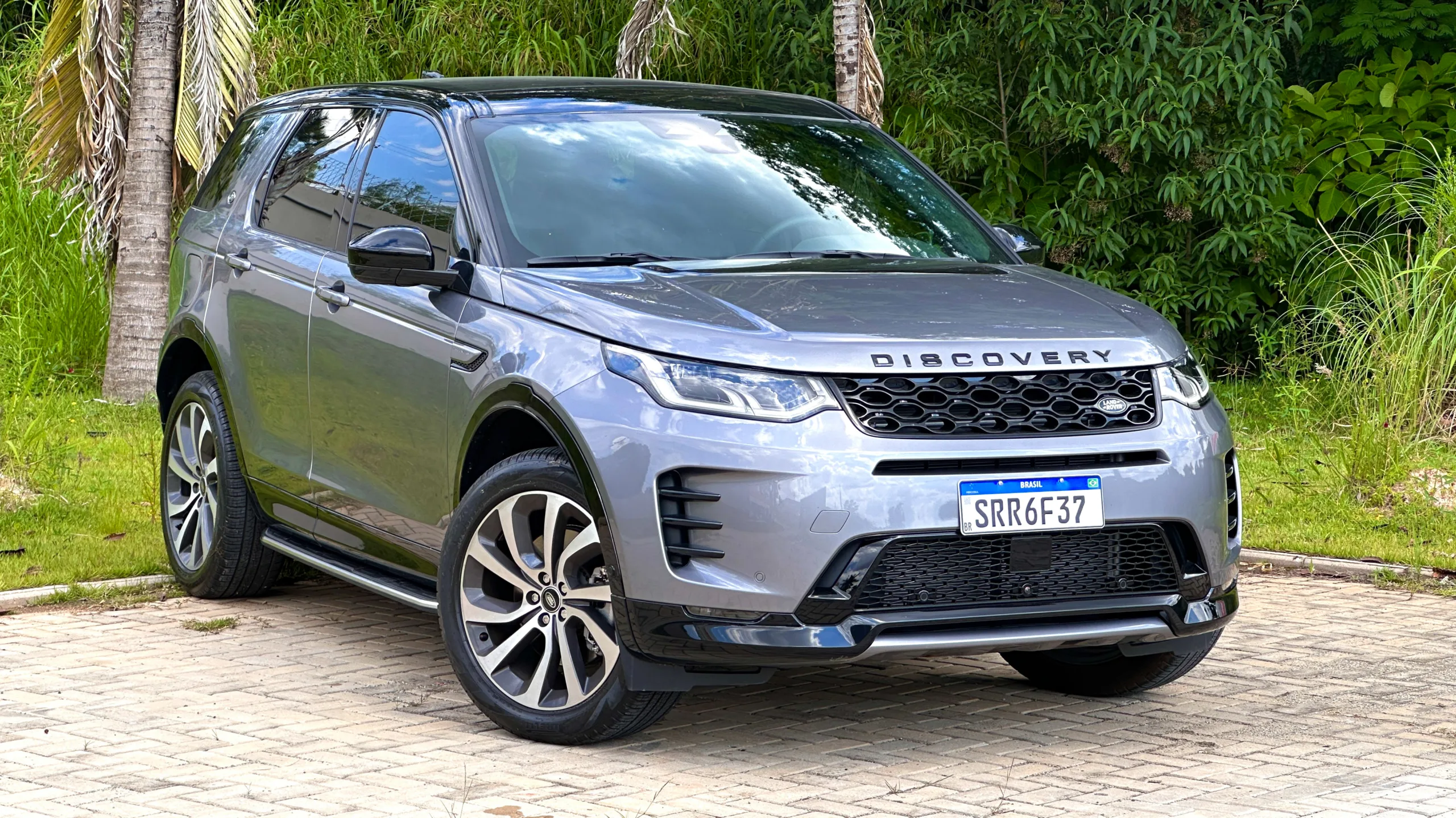 Land Rover Discovery Sport SE Dynamic flex cinza com teto preto parado em frente a um matagal