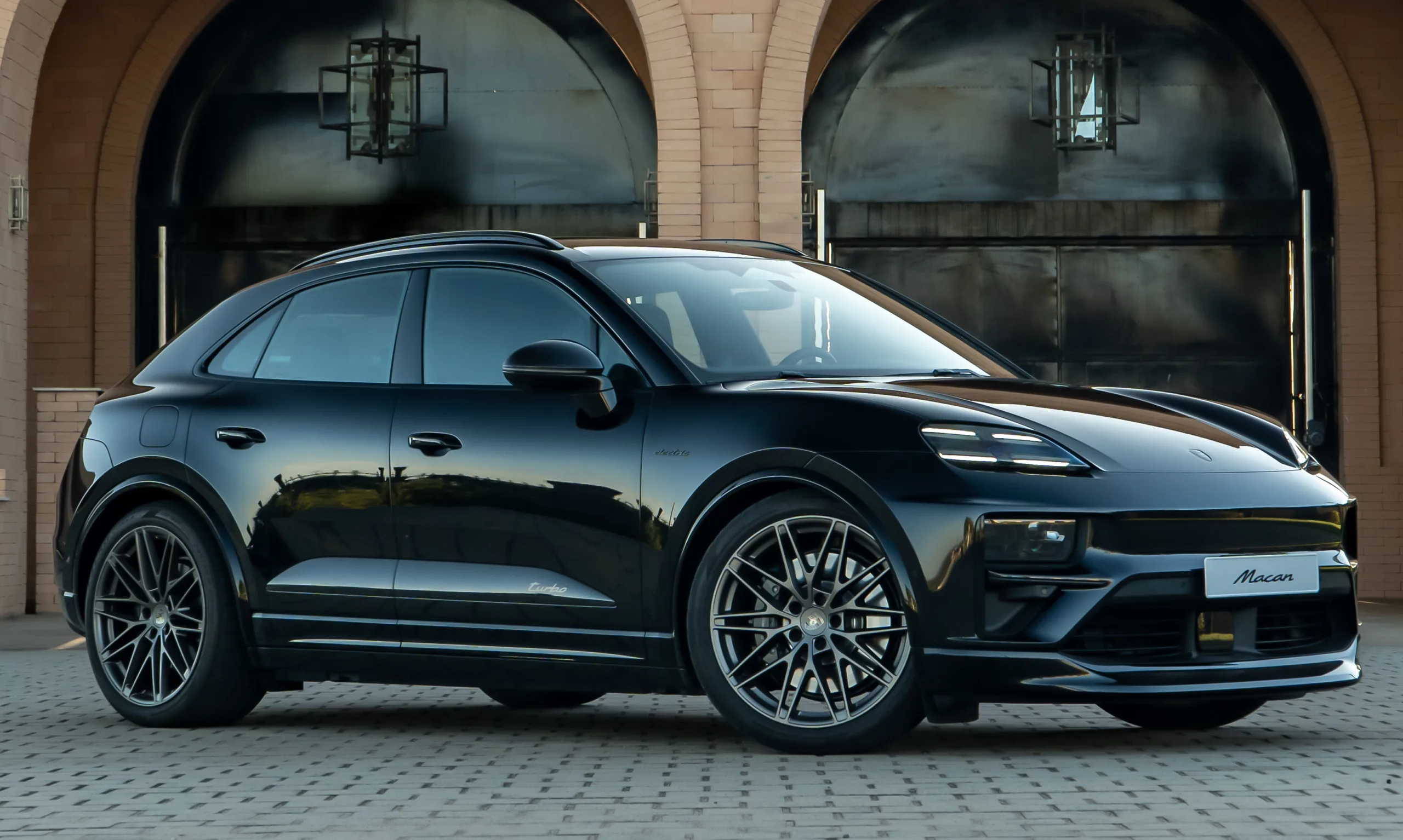 Novo Porsche Macan elétrico Turbo preto, visto de frente e portões ao fundo