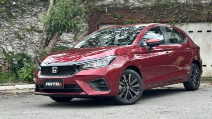 Honda City Hatch Touring 2025 vermelho de dianteira estacionado em frente a um portão branco