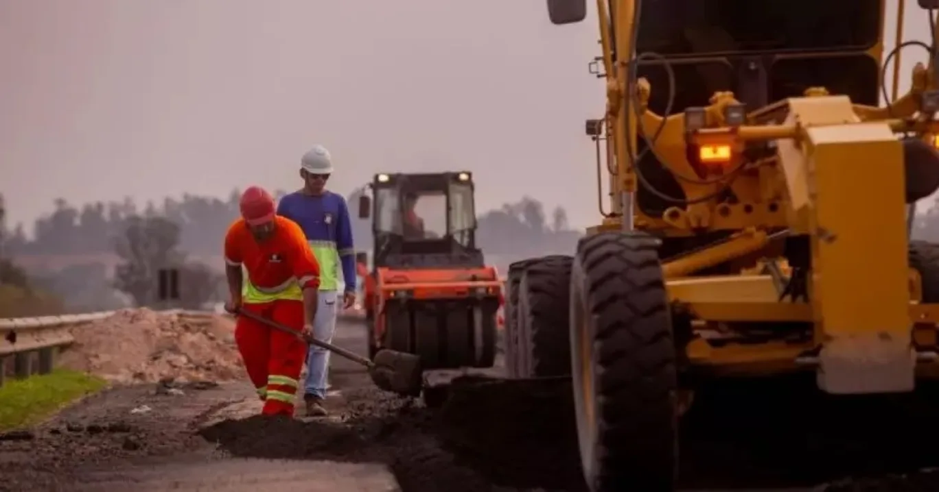 Homens uniformizados fazendo obras na pista com trator e mais máquinas em funcionamento