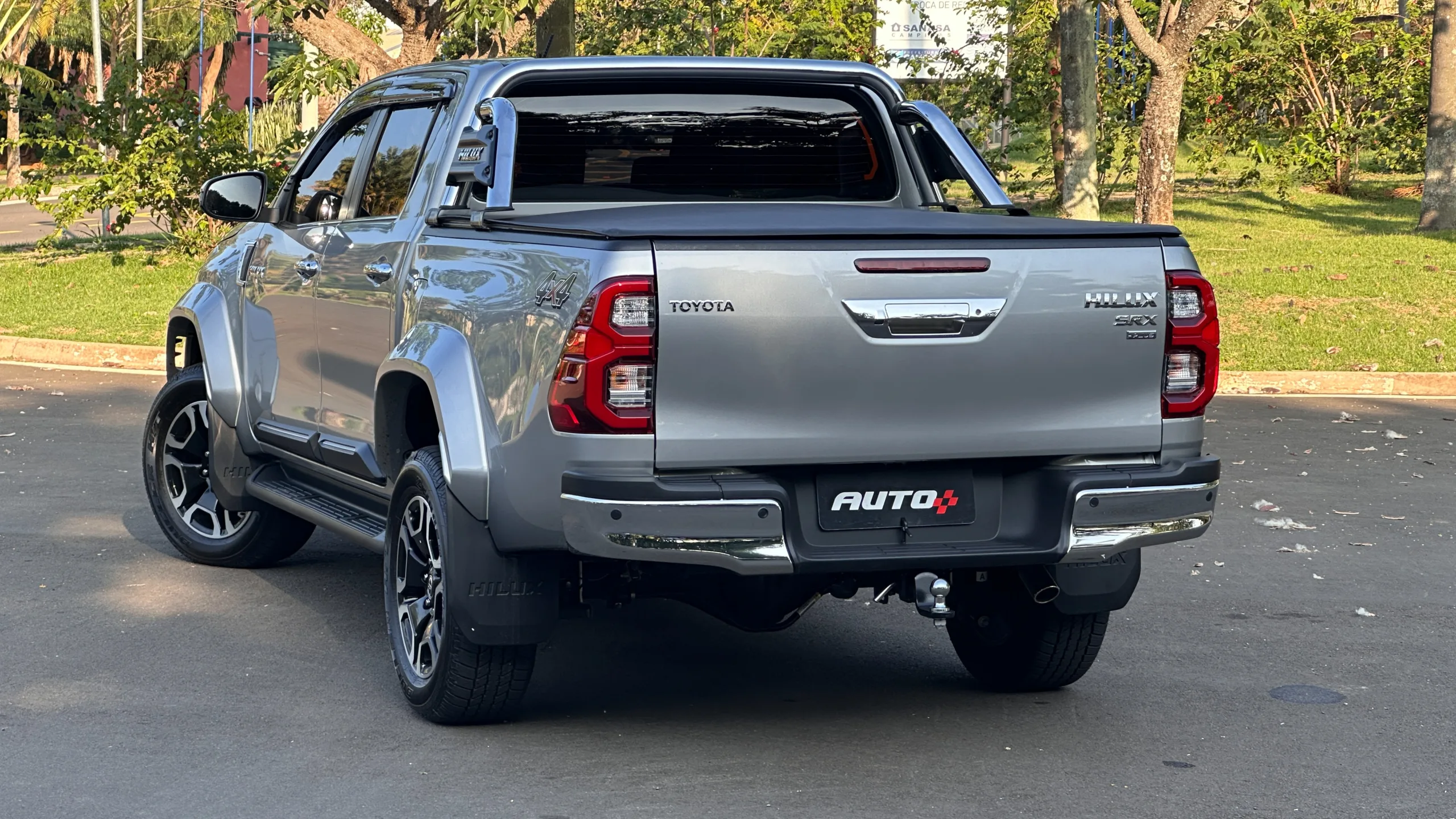 Toyota Hilux SRX Plus prata parada de traseira em um estacionamento com uma floresta ao fundo