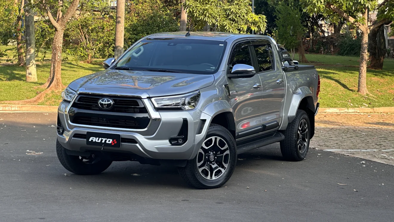 Toyota Hilux SRX Plus prata parada de frente em um estacionamento com uma floresta ao fundo