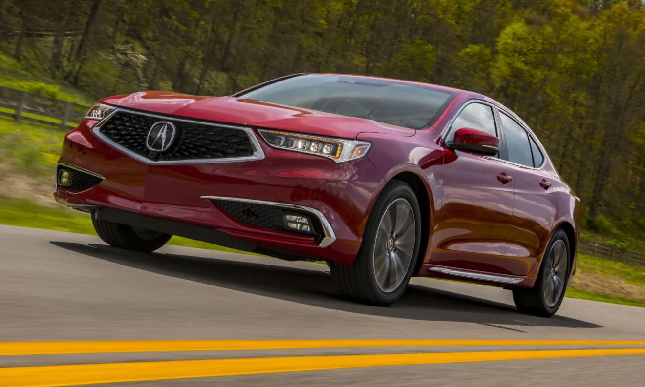 Acura TLX vermelho com faróis acesos, visto de frente e andando em rodovia