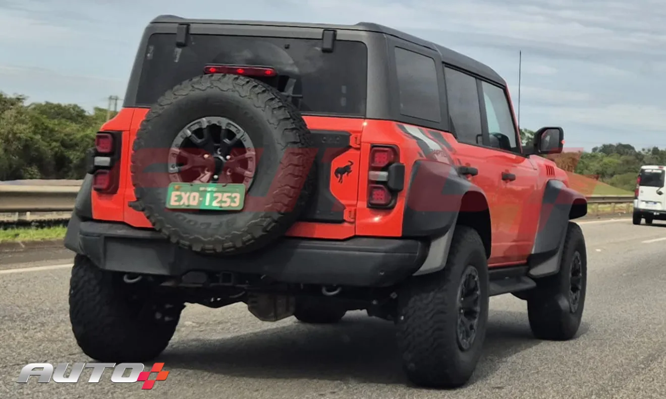 Ford Bronco Raptor laranja com partes pretas, visto de trás em uma rodovia