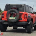 Ford Bronco Raptor laranja com partes pretas, visto de trás em uma rodovia