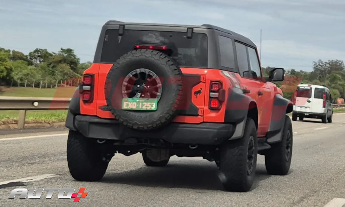 Ford Bronco Raptor laranja com partes pretas, visto de trás em uma rodovia