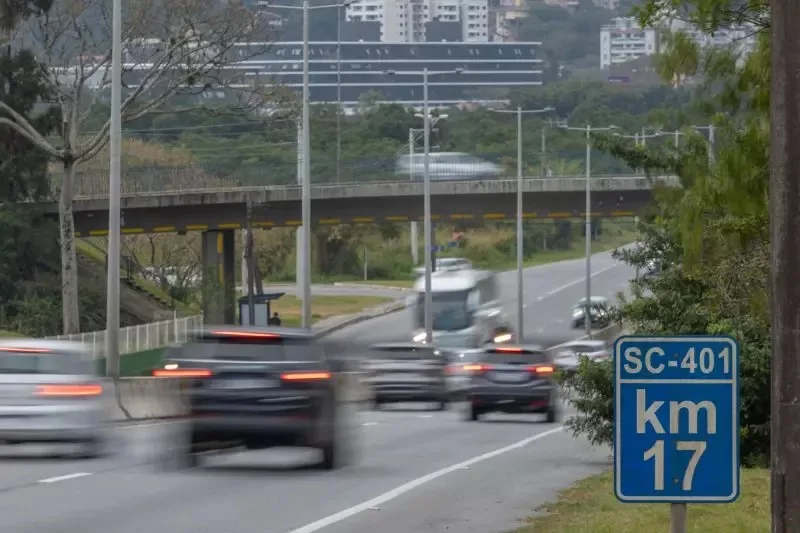 Trecho movimentado da Sc-401 com ônibus claro e faróis acesos de um lado e carros escuros em outro ângulo