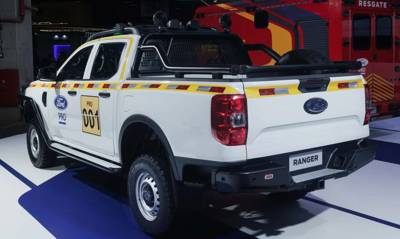 Ford Ranger Minera branca com adesivos amarelos, vista de trás e ao lado de uma ambulância vermelha