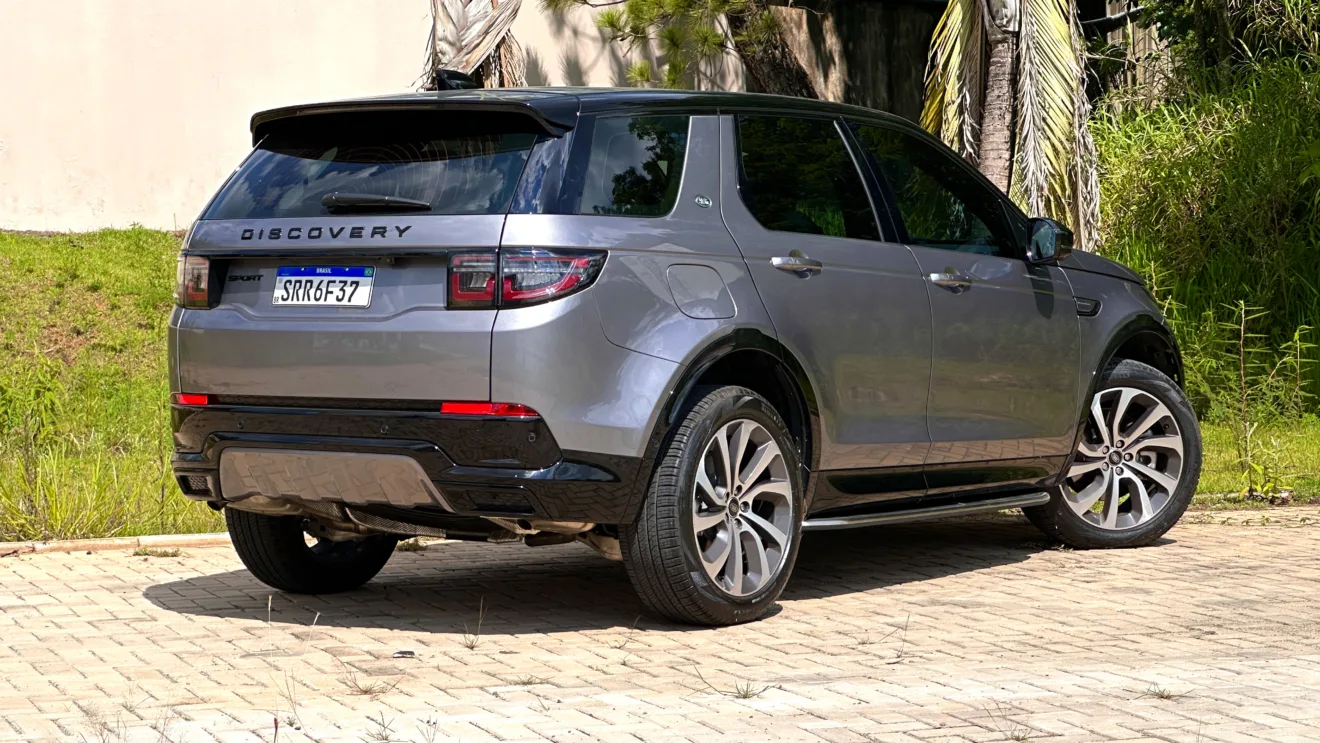 Land Rover Discovery Sport SE Dynamic flex cinza com teto preto parado de traseira com palmeiras ao fundo