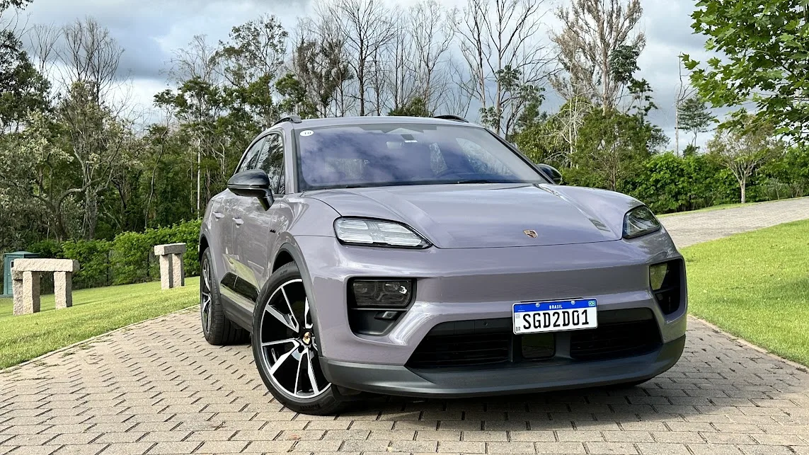 Porsche Macan elétrico roxo de frente com árvores, grama e pedras ao fundo 