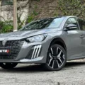 Peugeot 208 GT 2025 cinza visto de cima com portão branco e árvores ao fundo