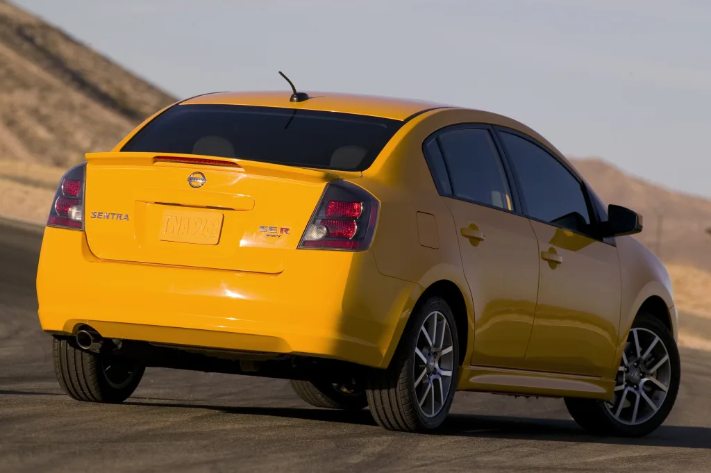 Nissan Sentra SE-R Spec V amarelo de traseira no asfalto com montanhas ao fundo