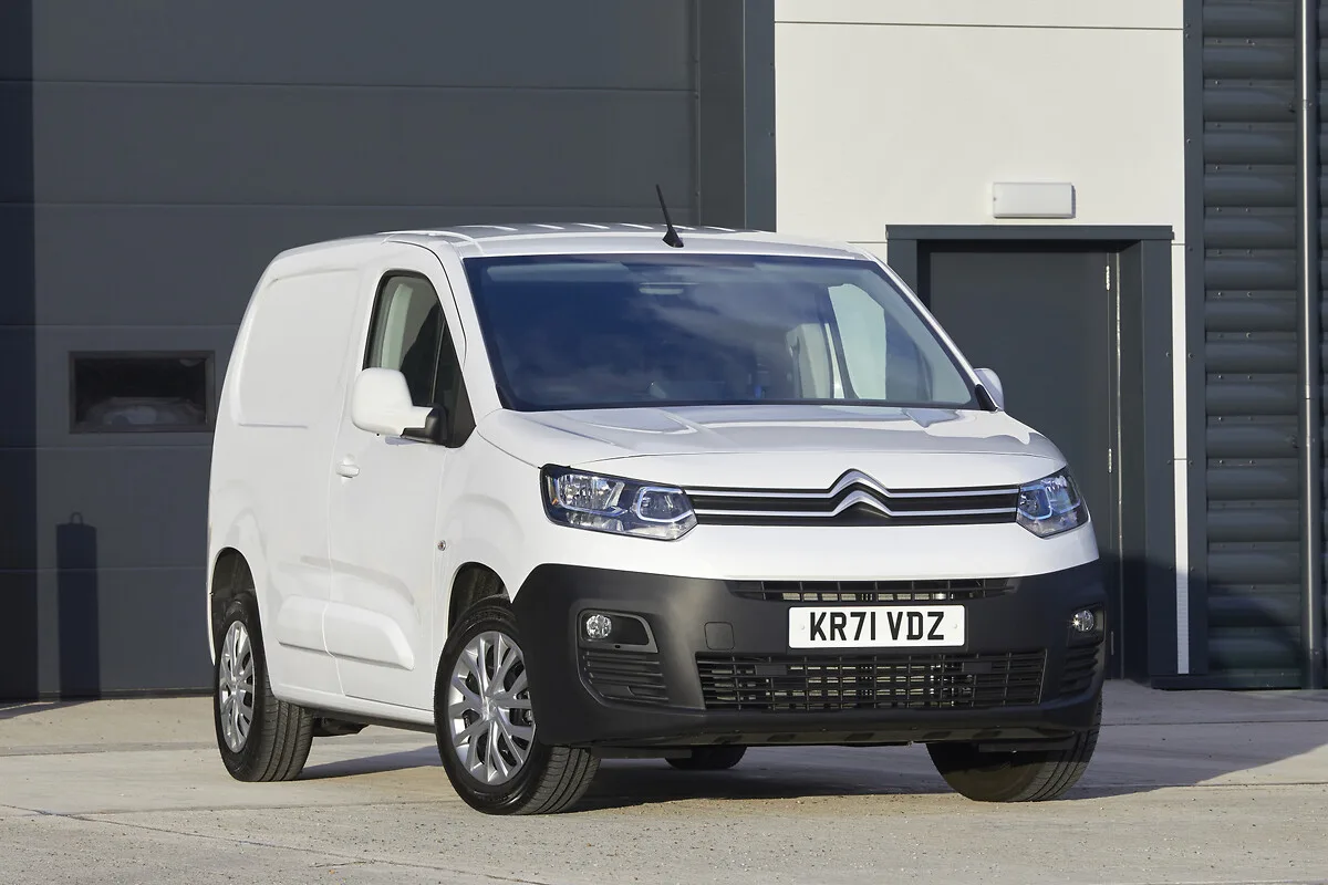 Citroën Berlingo branco com para-choque preto estacionado de frente a um galpão