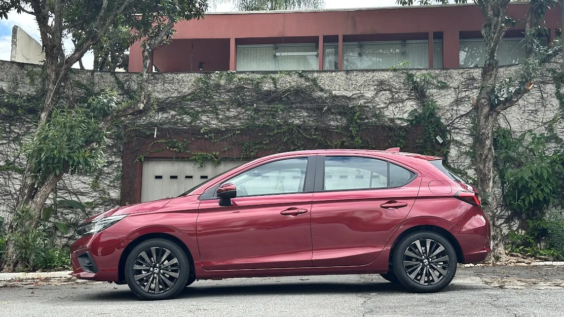 Honda City Hatch 2025 vermelho parado de lateral em frente a um portão branco