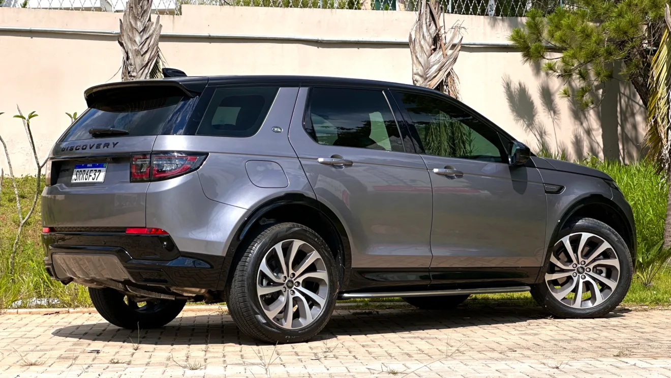 Land Rover Discovery Sport SE Dynamic flex cinza com teto preto parado de traseira com palmeiras ao fundo