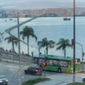 ônibus elétrico verde em uso em Florianópolis, visto lateralmente com carros e mar ao redor