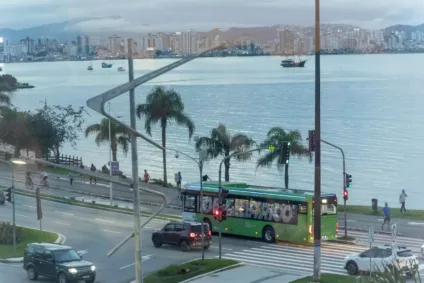 ônibus elétrico verde em uso em Florianópolis, visto lateralmente com carros e mar ao redor