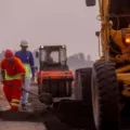 Homens uniformizados fazendo obras na pista com trator e mais máquinas em funcionamento