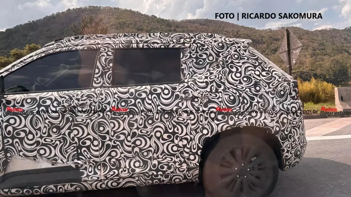 Protótipo do Honda WR-V 2026 com camuflagem branca andando em uma estrada, com montanha ao fundo e foco na traseira