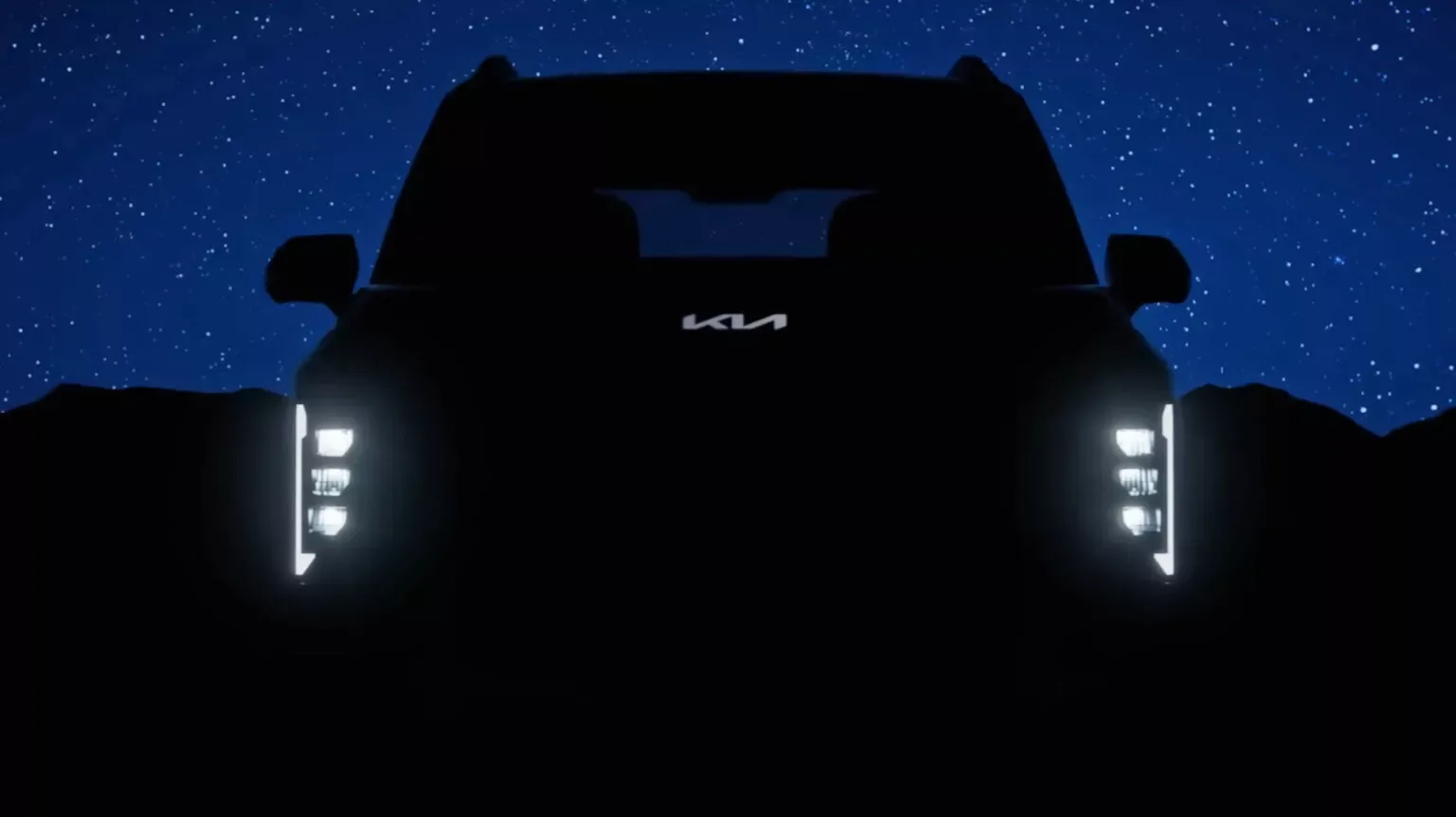 Teaser do Kia Syrons com os faróis e logo da Kia iluminados com fundo azul