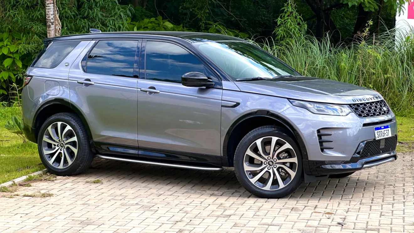 Land Rover Discovery Sport SE Dynamic flex cinza com teto preto parado em frente a um matagal