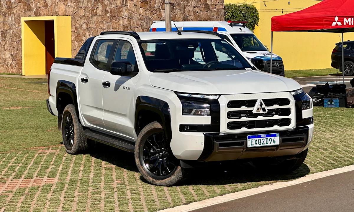 Mitsubishi Triton Katana branca de frente com detalhes pretos em um estacionamento gramado com detalhes amarelos ao fundo