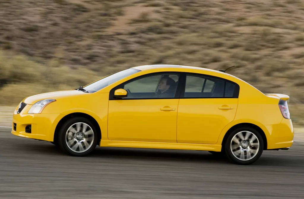 Nissan Sentra SE-R Spec V amarelo de lado andando no asfalto com montanhas ao fundo