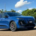 Audi Q6 e-tron azul parado de frente no asfalto com árvores ao fundo