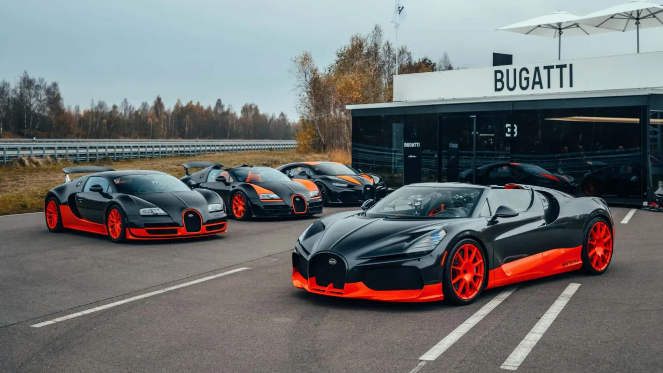 Esportivos da Bugatti vistos de frente, pintados de preto e laranja com uma pista ao fundo