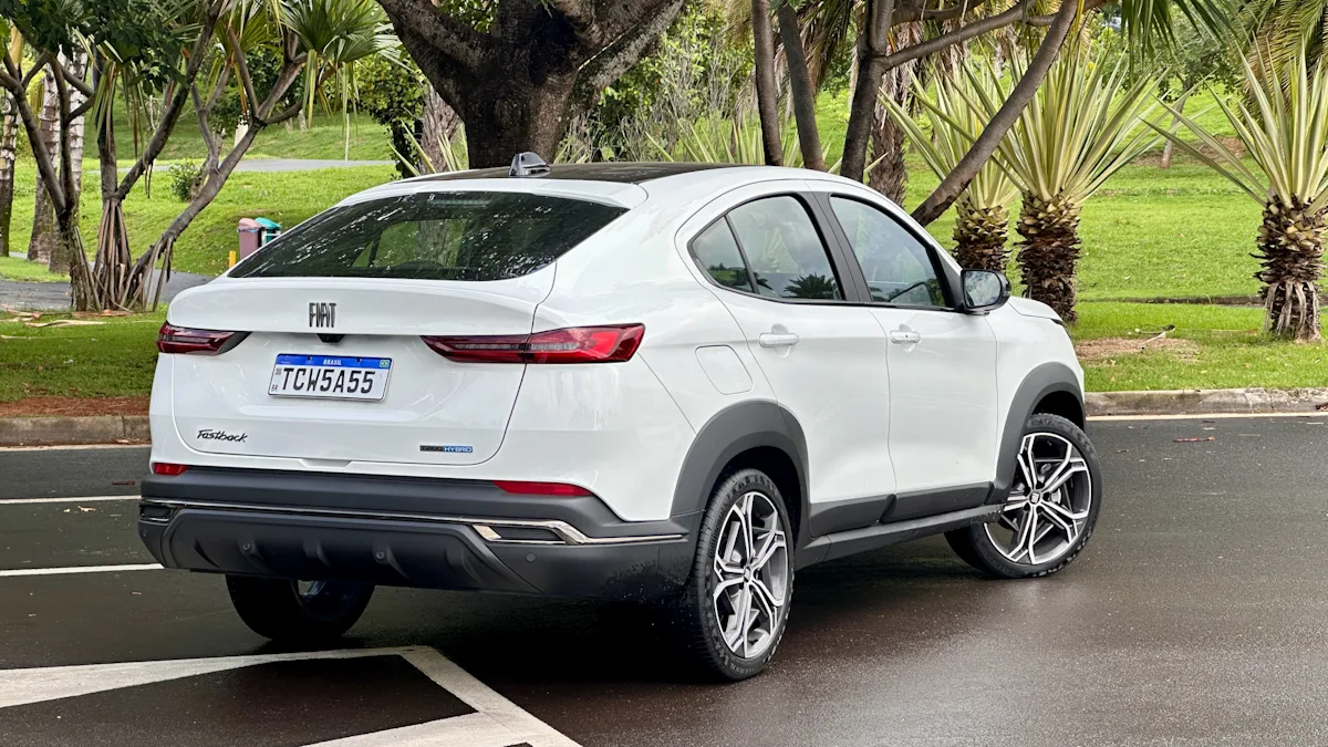 Fiat Fastback Hybrid branco de traseira em um estacionamento molhado com uma floresta ao fundo